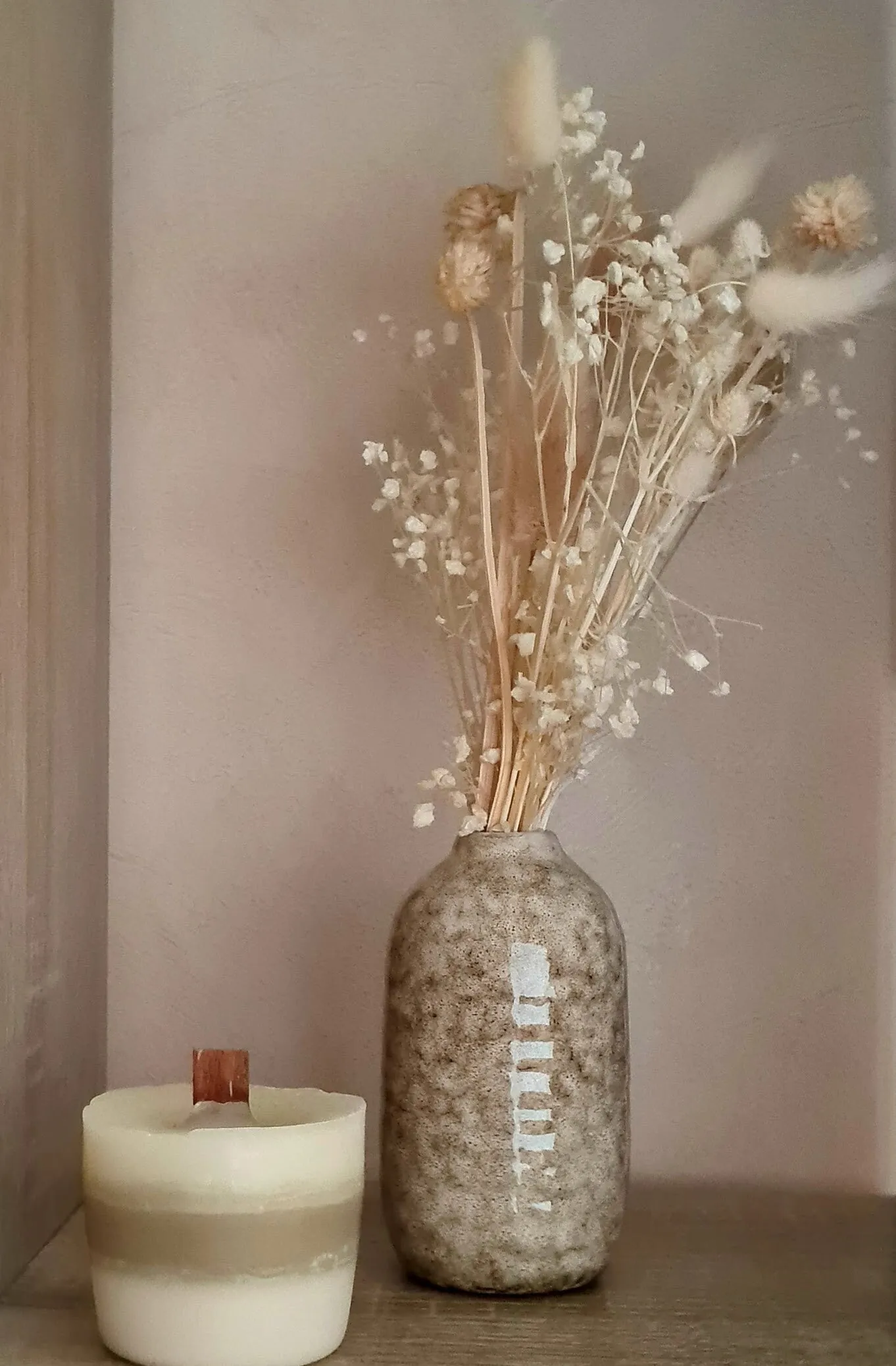 Un bouquet de fleurs séchées dans un vase, à côté d’une bougie